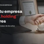 Apretón de manos sobre un contrato en un despacho al cerrar la venta de una empresa a través de una holding
